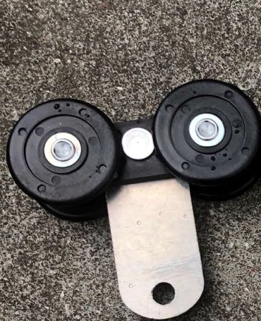A roller assembly with black wheel ends, a wheel carrier, and a metal connecting plate with a mounting hole, photographed on a concrete surface